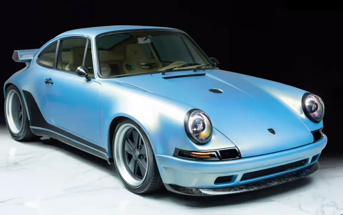 Porsche 911 restaurado em azul-claro perolado, visto de frente em três quartos sobre piso de mármore branco